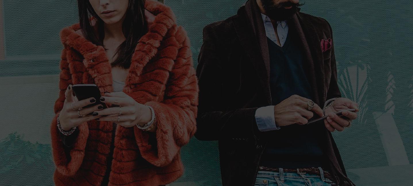 Blog Overview Hero Two people standing side by side - one in orange fur coat using phone, one in dark suit checking wallet.